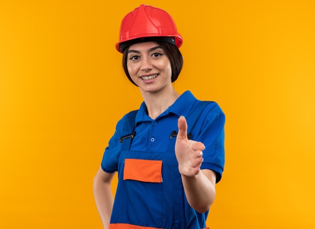 Sonriendo mirando a la cámara mujer joven constructor en uniforme sosteniendo la mano a la cámara