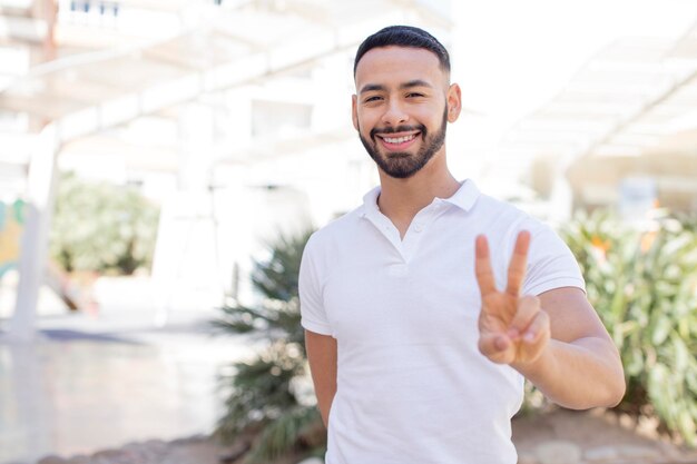 sonriendo y mirando feliz despreocupada y positiva gesticulando victoria o paz con una mano