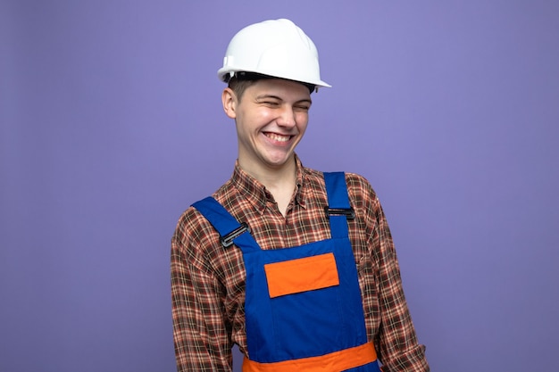 Sonriendo mirando de lado joven constructor masculino vistiendo uniforme