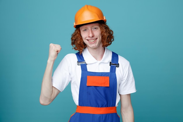 sonriendo mostrando sí gesto joven constructor hombre en uniforme aislado sobre fondo azul.