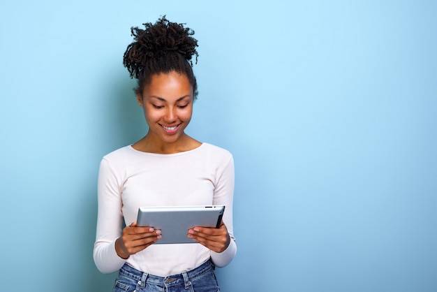 Sonriendo mulata mujer de pie con ipad mirando la pantalla y sonríe feliz