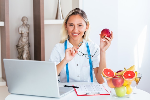 Foto sonriendo nutricionista en oficina sosteniendo una fruta