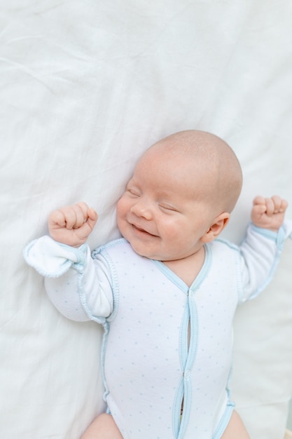Sonriendo o riendo en un sueño, un bebé recién nacido duerme durante siete días en una cuna en casa sobre una cama de algodón, primer plano.