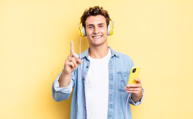 Sonriendo con orgullo y confianza haciendo la pose número uno triunfalmente, sintiéndose como un líder. concepto de auriculares y teléfono inteligente