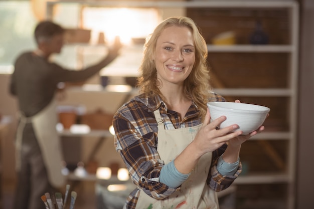 Foto sonriendo potter femenino control tazón en taller de cerámica