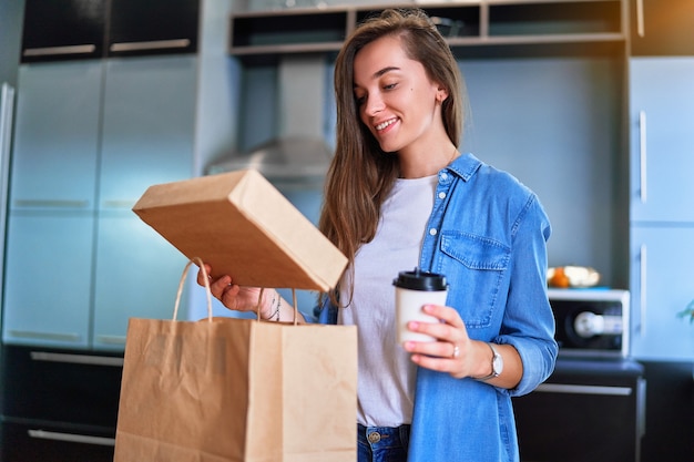 Sonriendo satisfecho feliz adulto casual alegre joven milenaria cliente recibió bolsas de cartón con comida para llevar y bebidas en casa. Concepto de servicio de entrega rápida