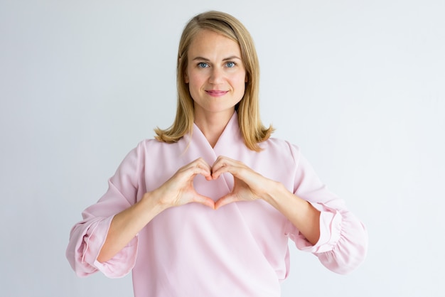 Sonriendo a la señora pacífica que muestra el corazón y que mira la cámara.