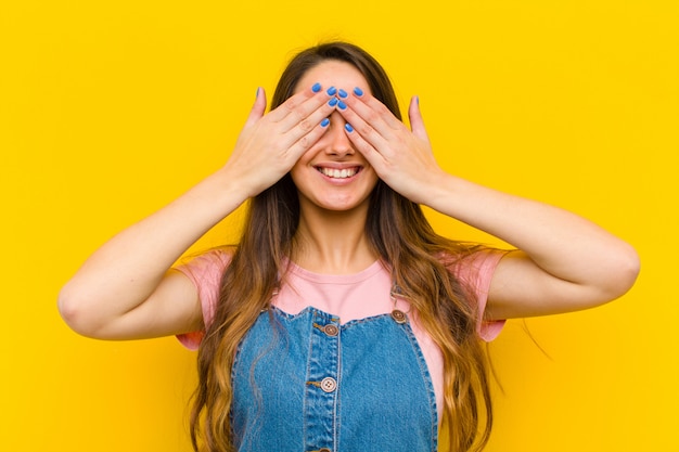 sonriendo y sintiéndose feliz, cubriéndose los ojos con ambas manos y esperando una sorpresa increíble