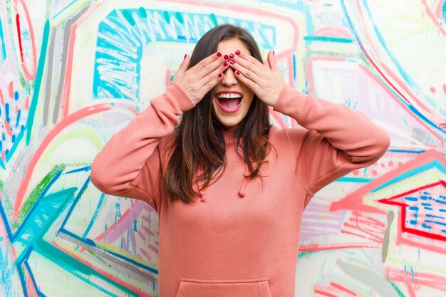 Foto sonriendo y sintiéndose feliz, cubriéndose los ojos con ambas manos y esperando una sorpresa increíble.