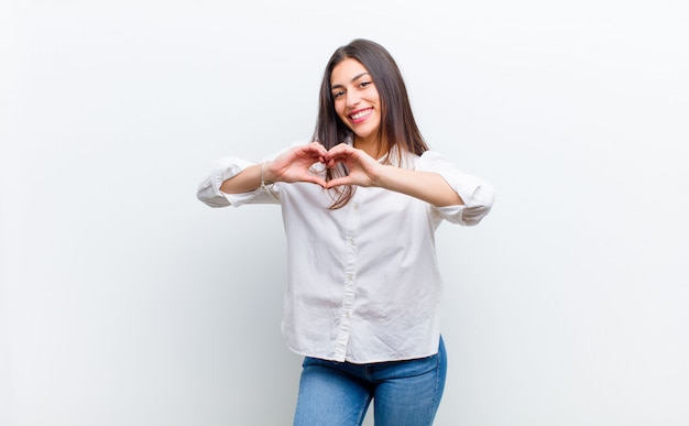 sonriendo y sintiéndose feliz, lindo, romántico y enamorado, haciendo forma de corazón con ambas manos