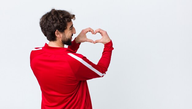 sonriendo y sintiéndose feliz, lindo, romántico y enamorado, haciendo forma de corazón con ambas manos