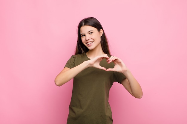 sonriendo y sintiéndose feliz, lindo, romántico y enamorado, haciendo forma de corazón con ambas manos