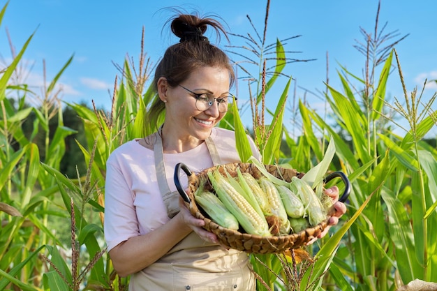 Sonriente agricultora con cesta de maíz recién recogido