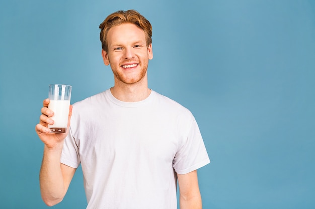 Sonriente alegre guapo joven barbudo de 20 años vistiendo ropa casual sosteniendo en la mano leche vegana