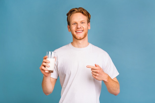 Sonriente alegre guapo joven barbudo de 20 años vistiendo ropa casual sosteniendo en la mano leche vegana