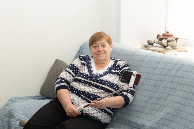 Sonriente anciana en casa con un teléfono móvil en las manos Emociones positivas Vida en el hogar