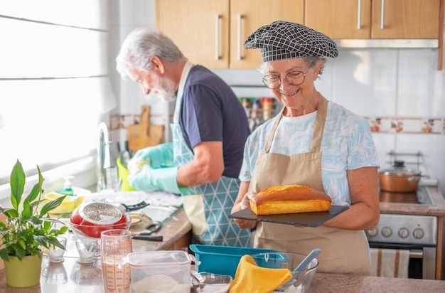 Sonriente anciana en la cocina casera sosteniendo una cocina casera recién horneada en casa para el concepto familiar