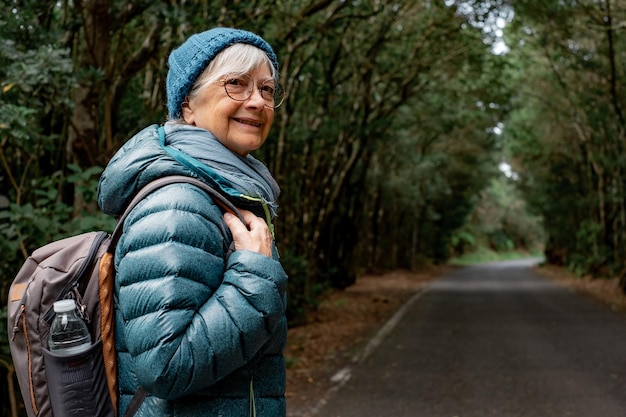 Sonriente anciana disfrutando de la libertad al aire libre caminando en un bosque de montaña Anciana alegre viajando en un parque con mochila