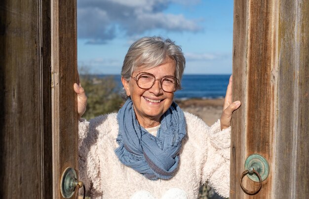 Sonriente anciana madura abriendo la puerta de madera de la casa del mar