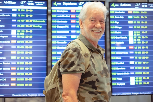 Sonriente anciano senior en el aeropuerto con equipaje esperando su puerta de salida del vuelo Concepto de viaje