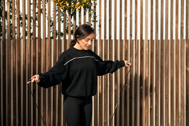 Sonriente atleta milenaria caucásica en ropa deportiva saltar a la cuerda haciendo ejercicio al aire libre