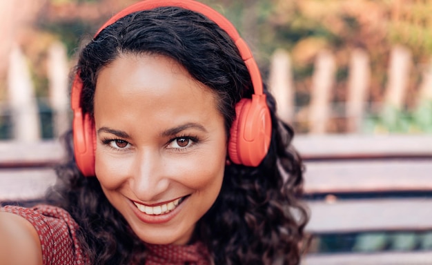 Sonriente atractiva mujer hispana tomando un selfie con auriculares retrato de hermosa dama mediterránea de cabello castaño