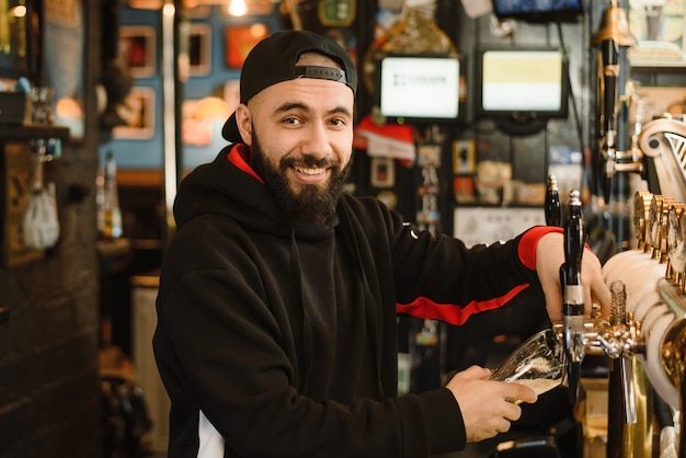 Sonriente barman barbudo vierte cerveza en un vaso