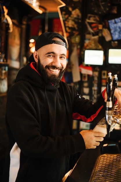 Sonriente barman vertiendo cerveza en un bar.