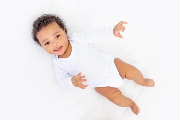 Sonriente bebé afroamericano en la cama blanca en el dormitorio riendo