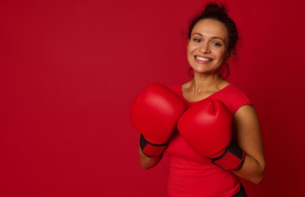 Sonriente boxeadora mujer bonita con guantes de boxeo rojos sonríe con dientes mirando a la cámara aislada sobre fondo de color con espacio de copia