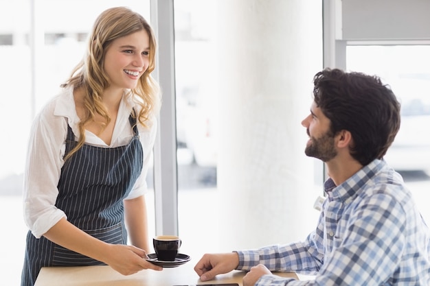 Sonriente camarera sirviendo un café al cliente