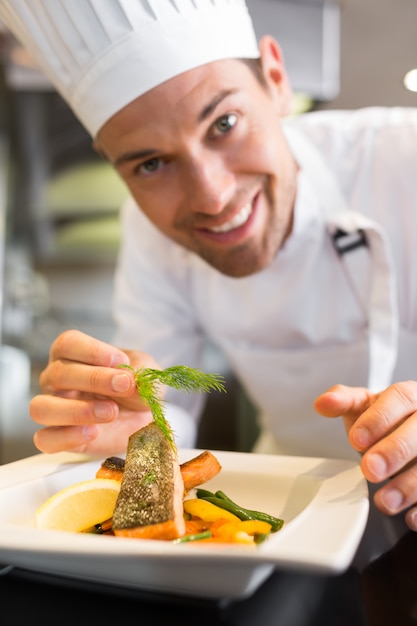 Sonriente chef masculino guarnición de alimentos en la cocina