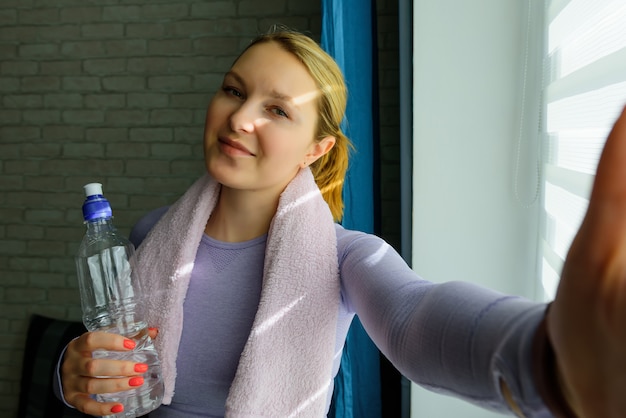 Sonriente chica atractiva fitness con toalla y botella de agua después del entrenamiento
