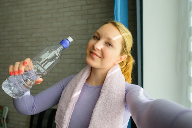 Sonriente chica atractiva fitness con toalla y botella de agua después del entrenamiento