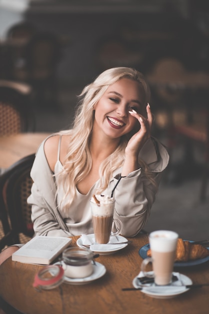 Sonriente chica rubia bebiendo café divirtiéndose en el café