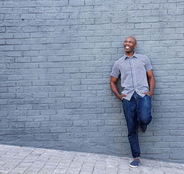 Sonriente chico africano apoyado contra la pared gris