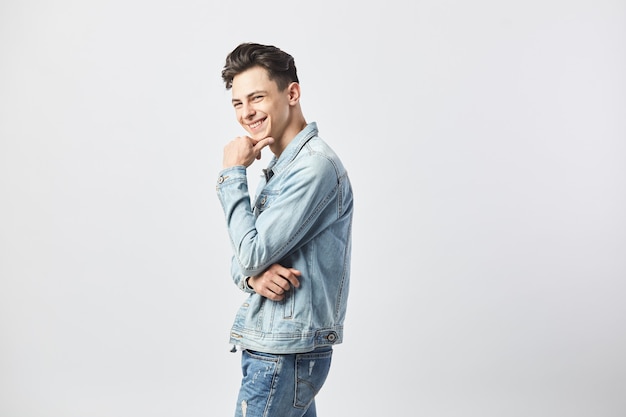 sonriente chico de pelo oscuro vestido con una camiseta blanca y una chaqueta de mezclilla