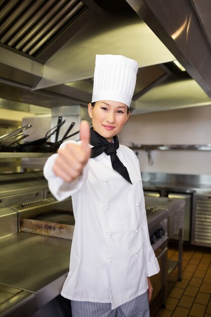 Sonriente cocinera gesticular pulgares arriba en la cocina