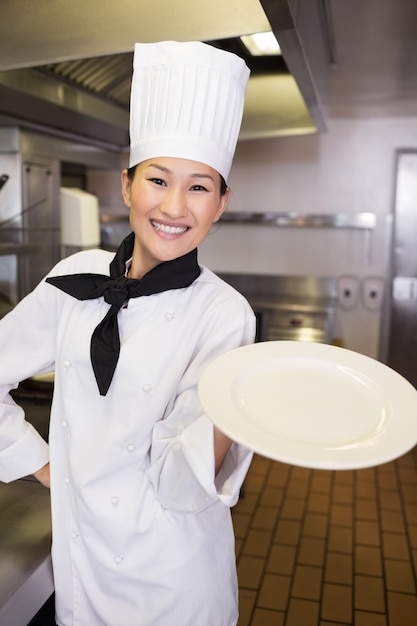 Sonriente cocinera sosteniendo un plato vacío en la cocina