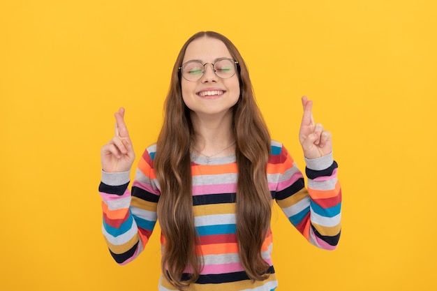 Sonriente colegiala soñadora nerd niño en anteojos para visión cruzó los dedos haciendo sueño de deseo