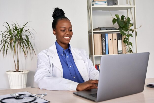 Sonriente doctora afroamericana gp usando computadora portátil en el lugar de trabajo