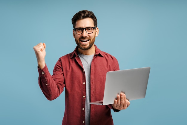 Sonriente emocionado hombre latino de mediana edad programador sosteniendo portátil usando computadora ganar dinero