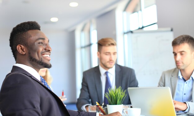 Sonriente empresario africano confiado en una reunión con colegas sentados en una mesa de conferencias en la oficina.