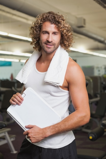 Sonriente entrenador guapo con portapapeles en el gimnasio