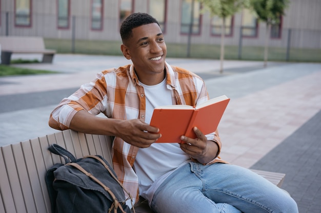 Sonriente estudiante afroamericano que estudia el aprendizaje de idiomas sentado en el campus universitario