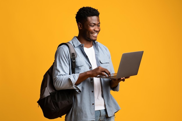 Sonriente estudiante afroamericano usando laptop