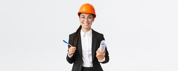 Sonriente y exitosa ingeniera de construcción en jefe empresaria con casco y traje con planos y contrato de firma de pluma con proveedor de construcción de fondo blanco