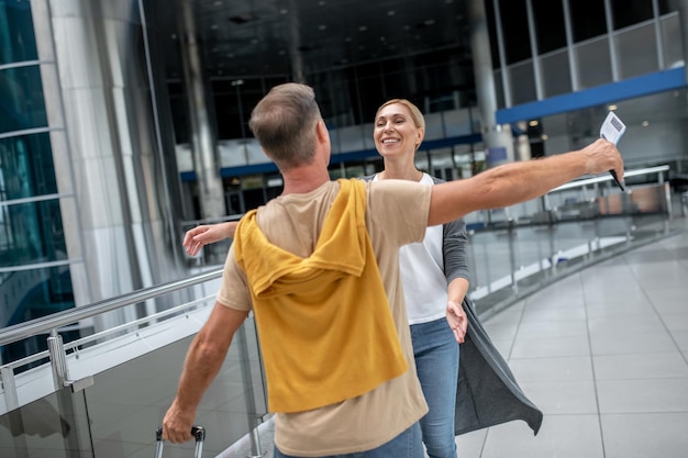 Sonriente, feliz y atractiva mujer caucásica rubia de mediana edad que se encuentra con un pasajero de la aerolínea en la terminal del aeropuerto