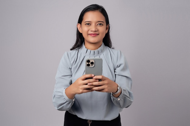 Sonriente feliz joven mujer de negocios asiática de 30 años usando un teléfono móvil y leyendo noticias aislado en fondo gris logro carrera riqueza concepto de negocio