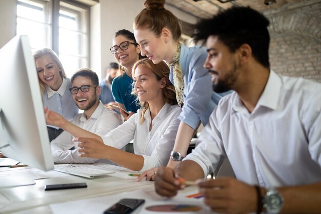 Sonriente gente de diseño trabajando juntos en un escritorio en la computadora en la oficina